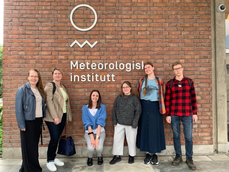 Cilvēku grupa stāv pie ēkas ar Meteoroloģiskā institūta zīmi.