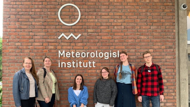 Cilvēku grupa stāv pie ēkas ar Meteoroloģiskā institūta zīmi.