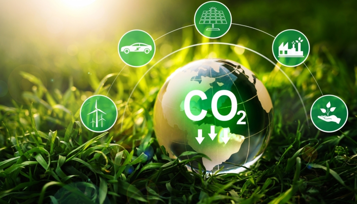 Zemes lodveida attēls zālē ar CO₂ simbolu un ikonām, kas attēlo atjaunojamo enerģiju un emisiju samazināšanu.