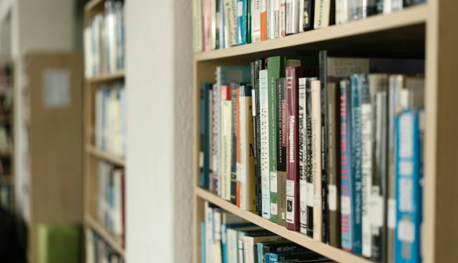 Grāmatu plaukti bibliotēkā, pilni ar dažādām grāmatām.